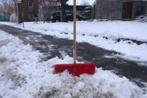 Ein frisch geräumter Gehweg im Winter. Eine rote Schneeschaufel steckt in dem entstandenen Schneeberg.